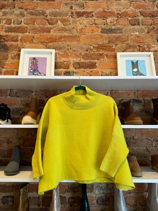 A bright yellow sweater hangs in front of a shoe shelf and a brick wall at Cate's Boutique